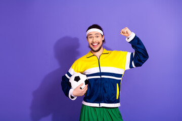 Cheerful male athlete in a colorful tracksuit holding a soccer ball and celebrating on a vibrant...