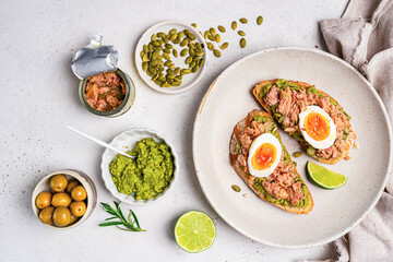 Tuna toast. Open sandwiches with whole grain bread, canned tuna, boiled egg, avocado and olives on white background. Healthy breakfast food, top view