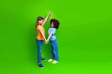 Two cheerful schoolgirls holding hands on a green background representing friendship, diversity, and positivity