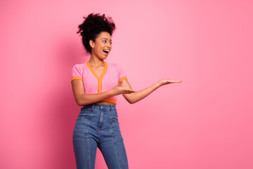 Charming young woman in casual outfit posing with a cheerful gesture against a pink background,...