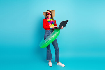 Joyful woman in summer outfit using a laptop in a fun setting with colorful accessories on a blue...