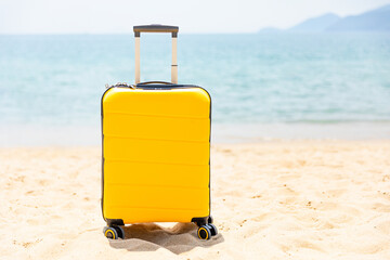 Yellow suitcase stands on white sandy beach with blue sea background. Travel insurance and touristic concept. Summer holidays lifestyle. Copy space. Mock up. High quality photo