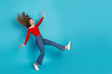 Excited young woman in casual red top and jeans enjoying a cheerful moment against a vibrant blue...