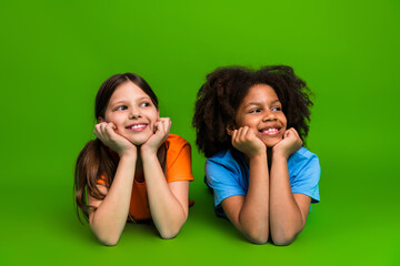 Two smiling young girls lying on a green background, expressing joy and friendship, wearing...