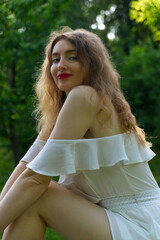 A woman with long, wavy hair and red lipstick smiles while wearing a white off-the-shoulder dress...