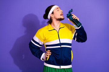 Young man enjoying a refreshing moment during exercise while holding a sporty water bottle against a purple background