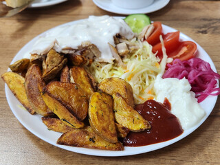 close-up of Chicken shawarma with fresh vegetables and cream sauce with Idaho potatoes on a plate on a wooden background