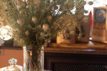 Bouquet of dried flowers and seed pods in clear glass vase with wooden mantel and blurred vintage...