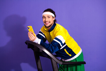 Young sporty man using smartphone while exercising on treadmill against purple background...