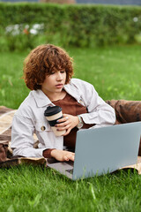 Young woman enjoys remote work in sunny park while sipping coffee and relaxing