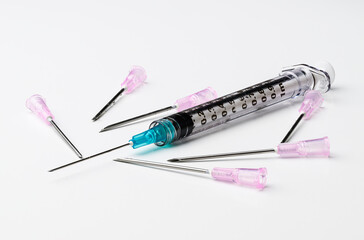 Medical syringe with blue needle and multiple pink needles on white background