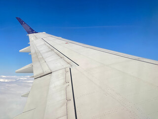 Airplane wing in the blue sky above the clouds