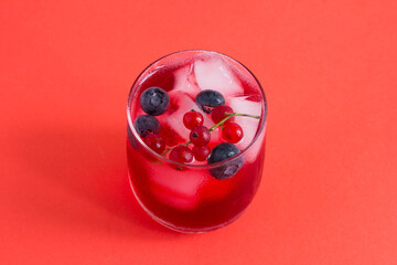 Cold lemonade or cocktail with red currants and blueberry in the drinking glass on a red background. Top view. Close-up.