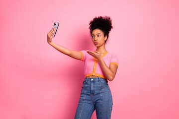 Stylish young woman in casual attire takes a selfie while posing playfully against a vibrant pink...