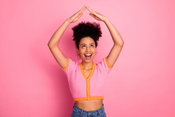 Cheerful young woman with hands forming shape on pink background portraying happiness and creativity