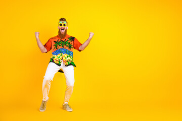 Colorful young man in tropical print shirt with bright style posing energetically in front of yellow background