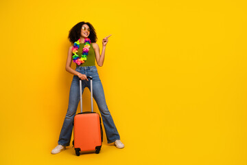 Stylish young woman with a travel suitcase against a bright yellow background, embodying confidence