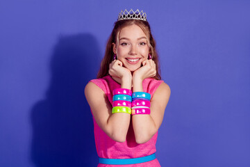 Smiling young woman in stylish pink dress with colorful bangles and tiara against a purple...