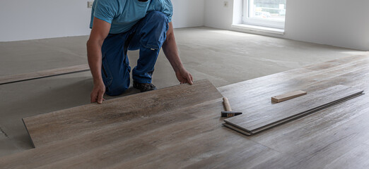 Floating floor work. The worker inserts the board of vinyl plank to the click system of Floating...
