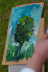 A person is skillfully painting a vibrant tree on a piece of cardboard, showcasing their artistic...