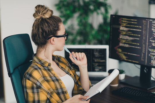 Young female programmer focusing on a coding project in a modern office workspace with multiple computer screens