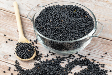 Bowl and spoon filled with black lentils on wooden surface