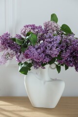 Bouquet of beautiful lilac flowers on wooden table near white wall