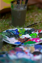On a table, there sits a vibrant palette of various paint colors alongside several brushes ready for artistic expression and creativity