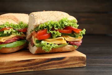 Pieces of tasty baguette sandwich with smoked sausage, cheese and vegetables on wooden table, closeup