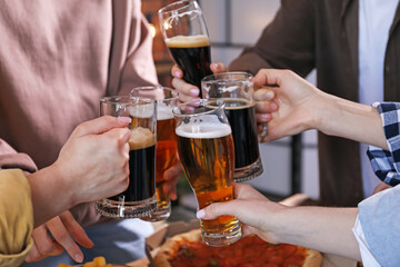 Friends clinking glasses of beer at table, closeup
