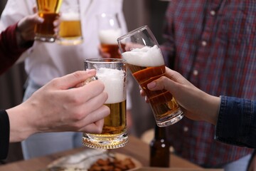 Friends clinking glasses of beer at table, closeup