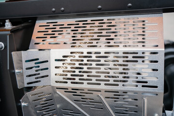 Perforated metal ventilation cover on industrial machine, protective panel with slotted openings used for heat dissipation, airflow control and mechanical component shielding