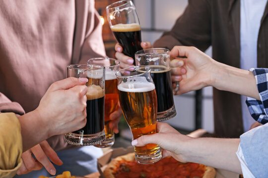 Friends clinking glasses of beer at table, closeup