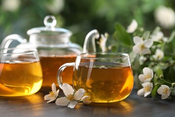 Tasty jasmine tea in cups, teapot and flowers on black table, closeup