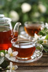 Tasty jasmine tea in cups, teapot and flowers on wooden table, closeup