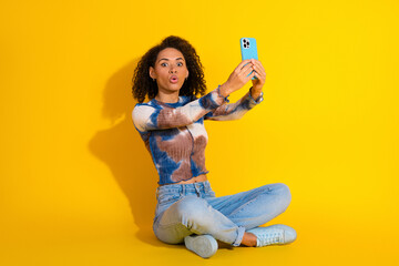 Young woman with curly hair taking selfie on yellow background, wearing trendy casual outfit and...