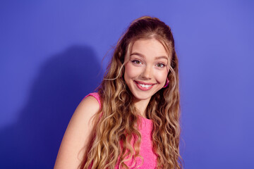 Young cheerful woman with long blonde hair in fashionable pink outfit posing against a vivid purple...