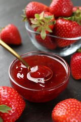 Tasty homemade strawberry jam and berries on black table, closeup