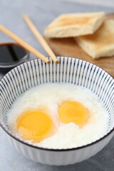 Traditional asian breakfast with half-boiled eggs in bowl, soy sauce, bread and chopsticks on grey table, closeup