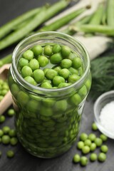Fresh green peas in pickling jar, pods and salt on black table, closeup
