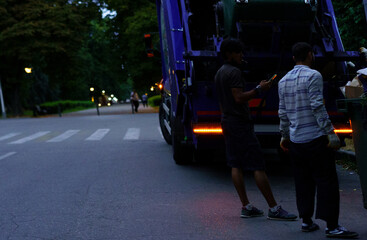 Workers collecting waste during early evening in a park setting, contributing to urban cleanliness...