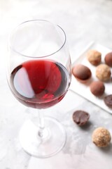 Red wine in glass and truffle bonbons on light table, selective focus