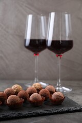 Tasty truffle bonbons and red wine on grey textured table, closeup