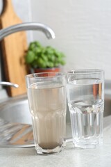 Glasses with clean and dirty water near sink indoors