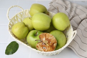 Spoiled apple and good ones in basket on white table, closeup