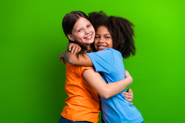 Two diverse young girls hugging happily in colorful casual outfits against a bright green background