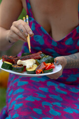 A woman is happily eating a delicious plate of food using chopsticks, showcasing her skill and enjoyment of the meal before her