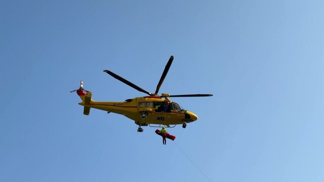 Positano,Italy-20 07 2025:Italian yellow rescue helicopter lifting rescuer and injured person on steel cable from seaside accident on the Amalfi Coast. Intense emergency action in dramatic coast