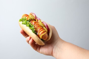 Woman with tasty hot dog on light grey background, closeup