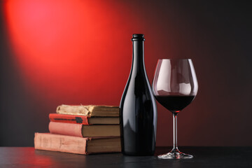 Tasty wine and stacked books on dark table in red light, closeup